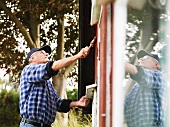 Älterer Mann streicht die Aussenfassade vom Sommerhaus