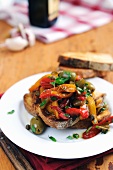 Bruschetta topped with red and yellow peppers, olives and capers