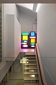 View of floating staircase treads and shelves of multi-coloured light boxes in designer apartment through glass balustrade