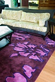Sofa mit Kissen im Bambusblatt-Design und auffällig gemusterter Teppich in Lila/Pink