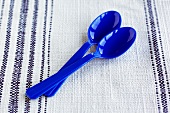 Two Blue Plastic Spoons on a Blue and White Linen Table Cloth