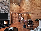 Minimalist living room with wood paneled walls and open fireplace under a TV on a natural stone wall