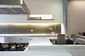 Gaskochfeld und Spülbecken in weißem Küchenblock gegenüber Küchenzeile mit indirekter Wandbeleuchtung