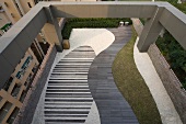 Stylische Dachterrasse mit verschiedenen Bodenbelägen und geschwungenem Grasstreifen