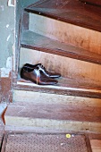 Men’s shoes threaded with spaghetti shoelaces on vintage wooden stairs