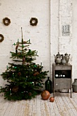 Christmas tree with lit candles next to small vintage cabinet against white wall in rustic atmosphere