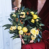Wreath of leaves and fruit held by woman in festive clothing