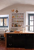 Kitchen counter with black cupboard doors below rustic shelves flanked by windows