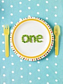 The word "one" spelled out with peas on a plate