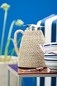Thermos jug with raffia cover on side table