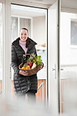 Junge Frau mit Jacke trägt einen Korb voller Gemüse und Obst