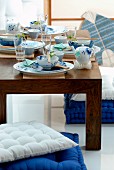 Asiatische Gedecke auf niedrigem Holztisch und Bodenpolster in Weiß und Blau