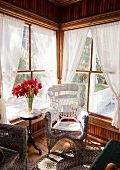 Weisser Korbstuhl am Fenster, Vase mit roten Blumen auf Beistelltisch