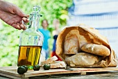 A jug of olive oil, ciabatta bread and olives on a wooden board