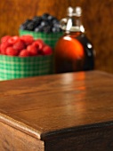 A wooden table with raspberries, blueberries and maple syrup in the background
