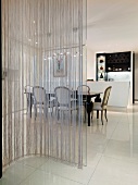 Curved glass pane with string curtain in front of a dining area in a modern living room with white floor tiles