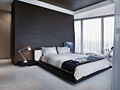 Frühstückstablett auf Doppelbett vor schwarz gefliestem Raumteiler in minimalistischem Schlafzimmer