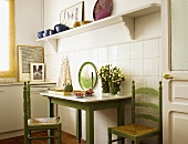 Schlichter Küchentisch mit grün lackierten Stühlen vor gefliester Wand unter weisser Wandkonsole
