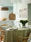 Kitchen table with tablecloth and wicker chairs in bright, country-house kitchen