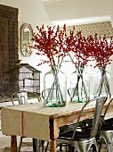 Glasvasen mit Beerenzweigen auf Tisch und Retro Metallstühle in schlichtem Wohnzimmer