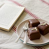 Petits fours next to cake forks on plate and open book on linen tablecloth