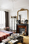 Bedroom with an antique coffee table on wheels next to a bed, fireplace and gold framed mirror