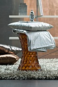 Cushion and throw with silver fabric covers on side table made from amber-coloured plastic and flokati rug