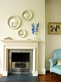 Open fireplace with traditional mantel and circular, framed mirrors on wall