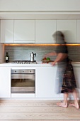Moderne Küche - Frau steht vor Küchenzeile mit weissen Ober- und Unterschränken