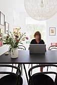 Frau arbeitet am Esstisch - Designer Hängelampe über schwarzem Tisch mit Blumenstrauss