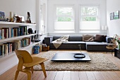Niedriger Bauhaus Stuhl aus Holz vor dunklem Bodentisch auf flokatiartigem Teppich und graues Designer Sofa am Fenster