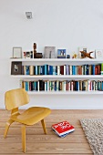 Low, wooden Bauhaus chair in front of white floating bookshelves