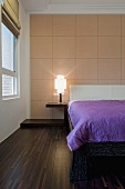 A screened wooden panel decorates a wall in a bedroom with a dark wooden floor