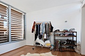 Clothes racks filled with stuff and shelves in a bedroom with large enclosed blind windows