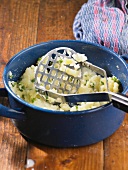 Mashed potatoes with herbs in a pot with a potato masher