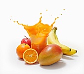 A splash of juice in a glass surrounded by oranges, bananas, mango and apple