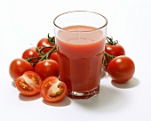 A glass of tomato juice surrounded by tomatoes