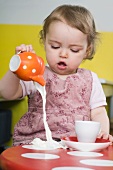 Kleines Mädchen verschüttet Milch auf dem Tisch