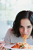 Young woman eating bowl of spaghetti with fork, portrait