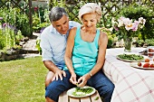 Mature woman peels pods, partner looks on