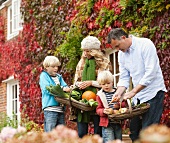 Familie mit Körben frisch geerntetem Herbstgemüse vor Haus