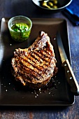 Grilled Rib-Eye Steak on a Dish with a Knife and Herb Sauce
