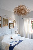 Helles Schlafzimmer - Zusammengebundene Zweige an Deckenleuchte über Bett mit weißem, filigranem Metallgestell an Wand unter gerahmten Bildern