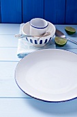 A blue and white plate, a bowl, a cup, cutlery and limes