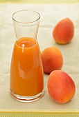 Apricot juice in a carafe with three whole apricots