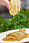 Salmon trout with a herb crust being drizzled with lemon juice