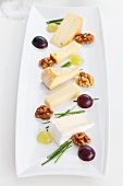A plate of cheese specialities with walnuts, chives and grapes