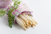Peeled white asparagus wrapped in a tea towel with carrot leaves