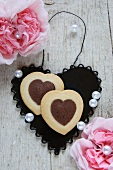 Bi-coloured heart-shaped biscuits on a black metal heart between paper carnations