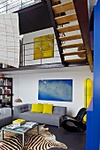Modernes, poppiges Wohnzimmer mit grauem Designersofa unter der Galerie und auffälligem Zebrateppich